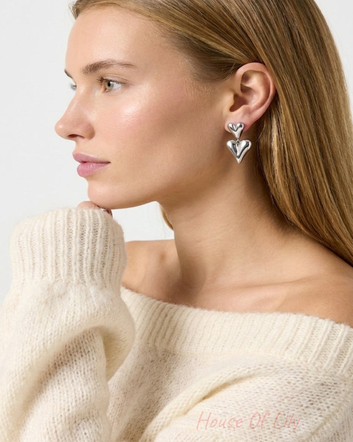 Profile of a woman wearing polished silver double heart drop earrings and a cream knit sweater.