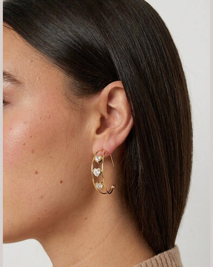 Chunky gold hoop earrings featuring three sparkly heart-shaped charms suspended between the dual bands.