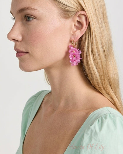 A woman wearing pink flower drop earrings with a gold hoop on her ear.