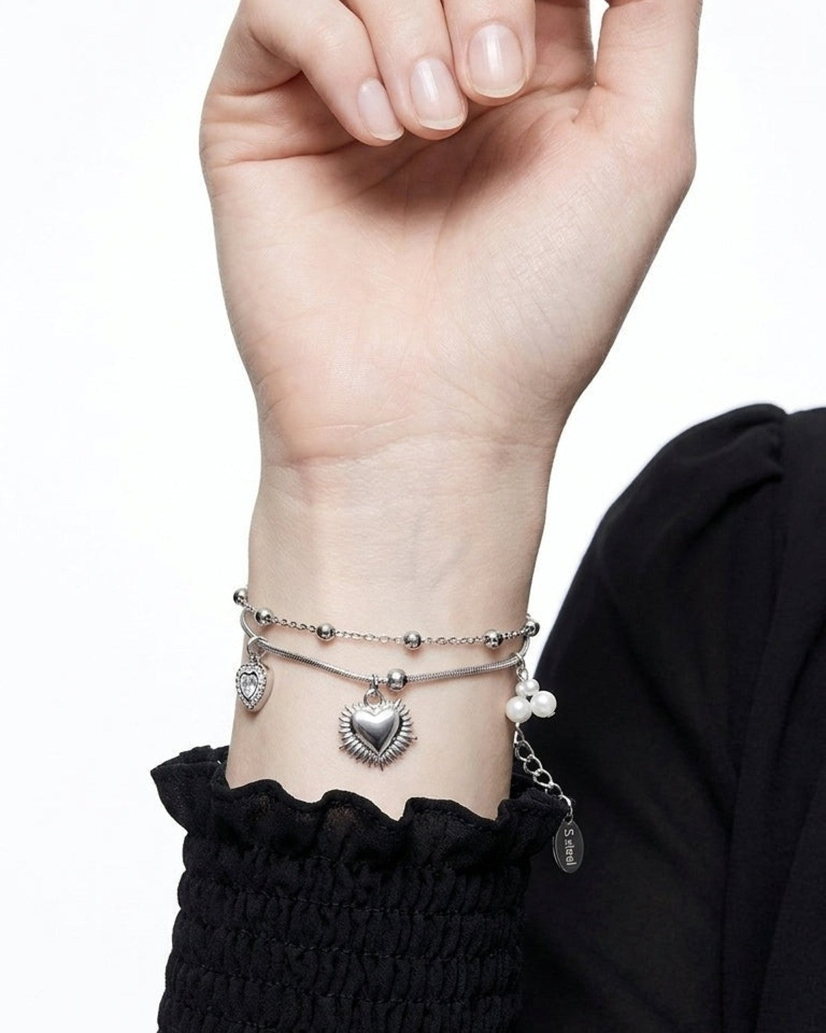 A silver-toned double chain bracelet featuring heart charms and small pearls worn on a wrist.