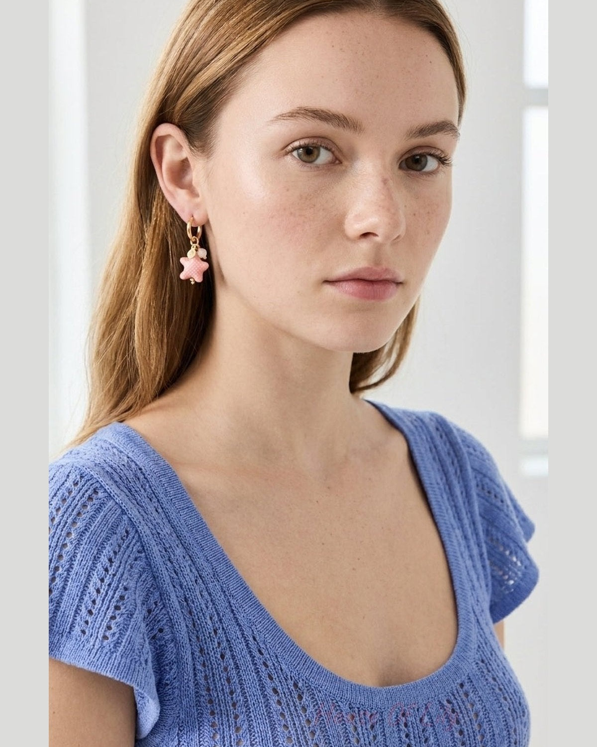 Azure Starfish Hoop: A gold hoop earring with a pink starfish-shaped charm worn on a woman.