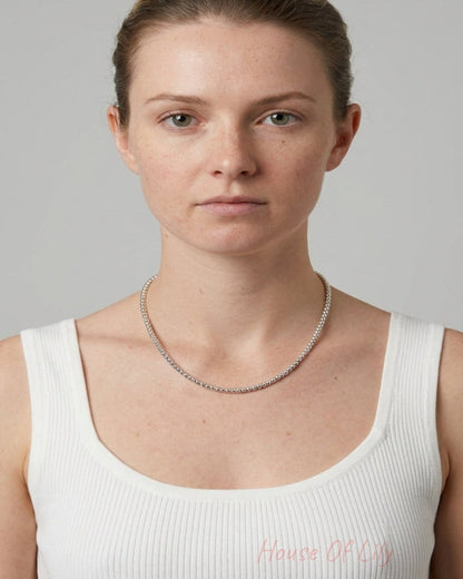 A person wearing a short, shiny silver beaded necklace with uniform round beads.