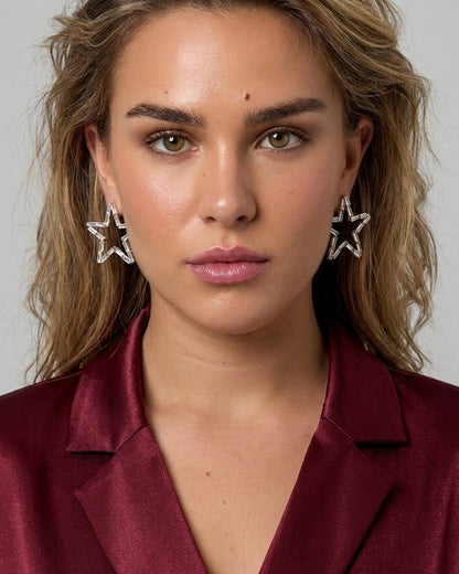 A woman wearing sparkly crystal star earrings with a maroon satin blazer.