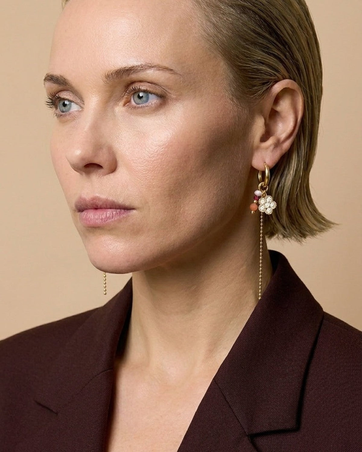 A woman wearing gold beaded flower earrings featuring small dangling charms and thin chains.