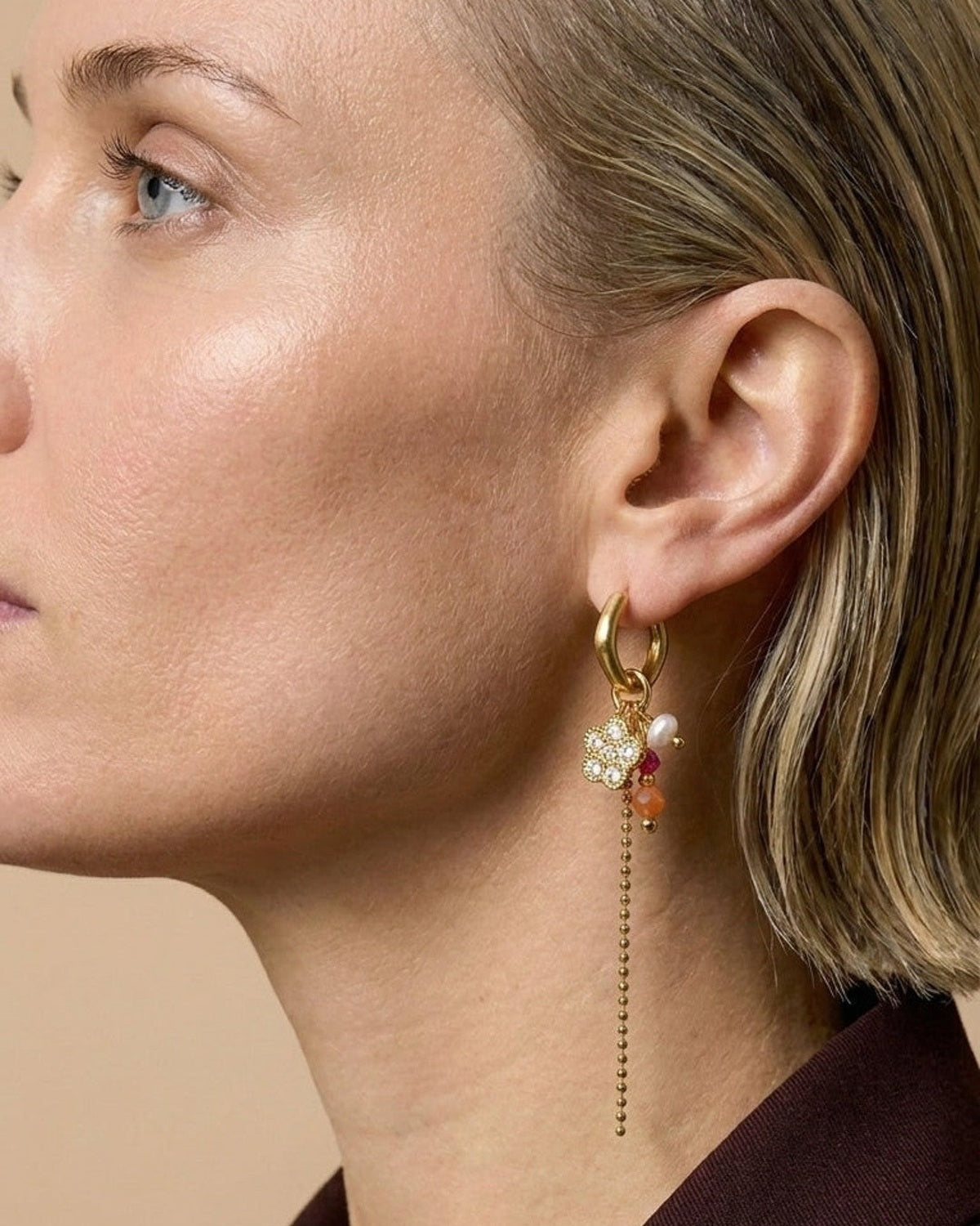 A woman wearing gold hoop earrings with a beaded flower charm and dangling beaded chain.