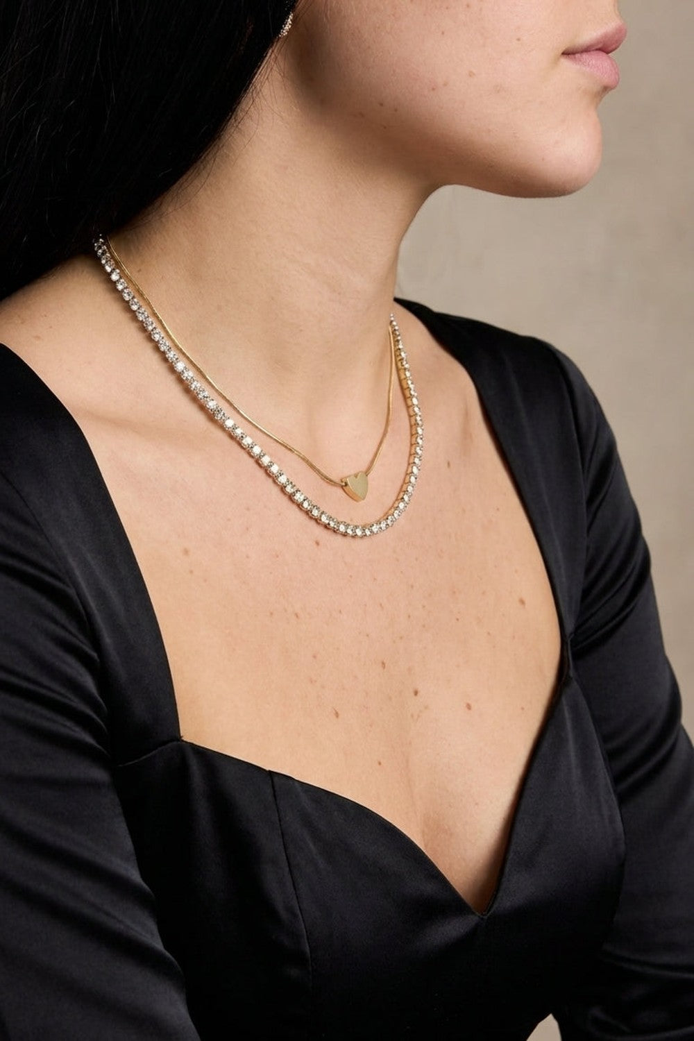 Layered gold heart necklace worn on a person, featuring a dainty heart pendant and a rhinestone tennis chain.