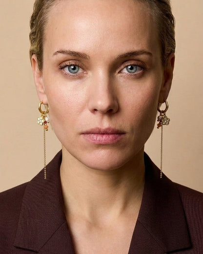 A woman wearing gold hoop earrings with beaded flower charms and a long dangling chain.