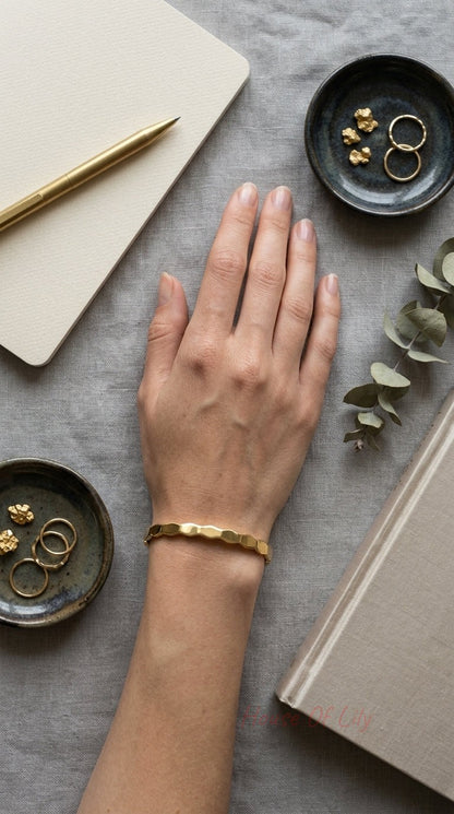 Minimalist gold bangle with a subtle, geometric, hexagonal link-style texture worn on a wrist.