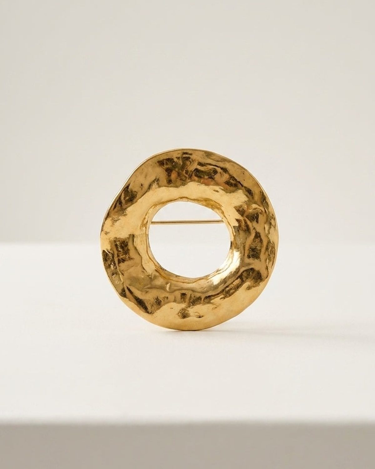 Textured gold circular brooch resting upright on a white surface.
