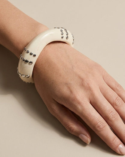 Thick, off-white resin bangle bracelet worn on a wrist, featuring embedded silver-tone metal studs in spaced rows.