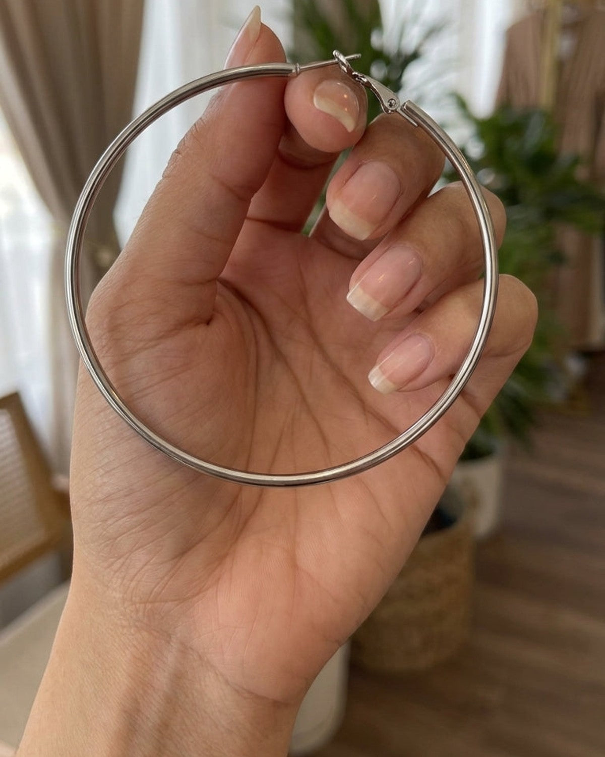 Large, thin silver metal hoop earring held upright in an open palm.