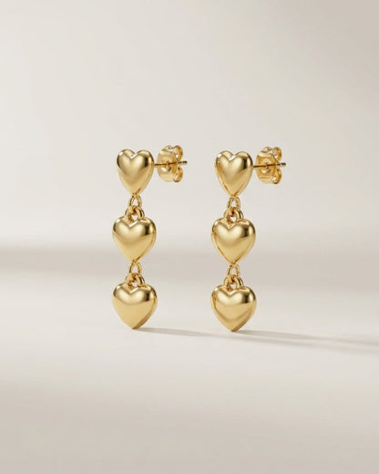 Gold heart dangle earrings, each featuring three puffed hearts linked vertically on post backs.