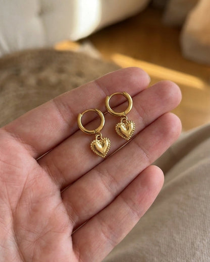 Heart Drop Earrings resting in a person's open hand, featuring small gold hoop earrings with beaded-edge heart charms.