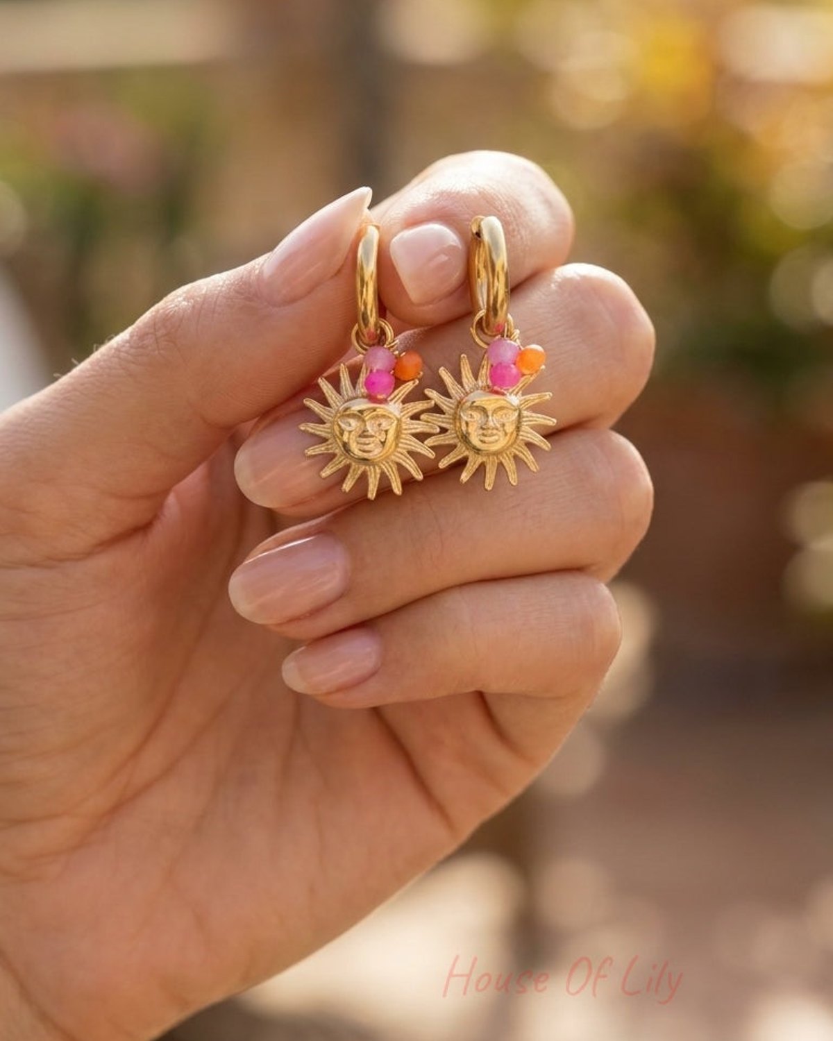 Two gold hoop earrings with dangling sun face charms and small pink and orange bead accents.