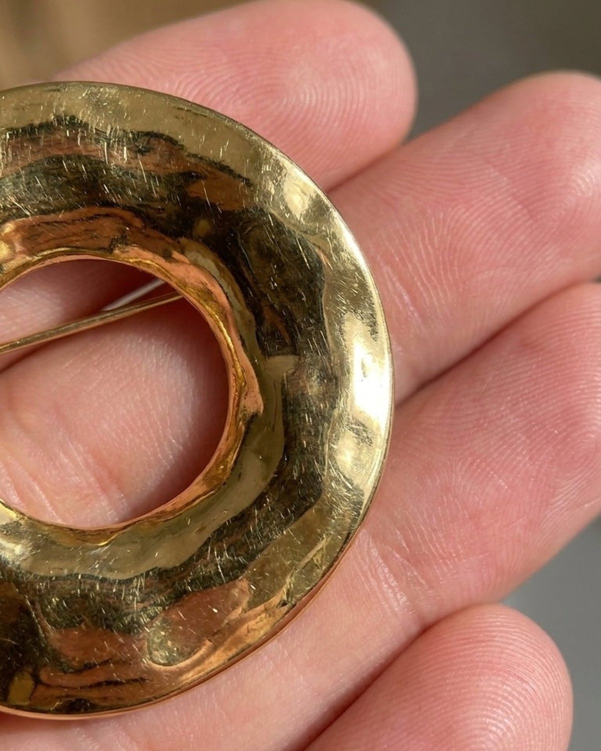A gold circular brooch with a textured, hammered surface rests on an open palm.