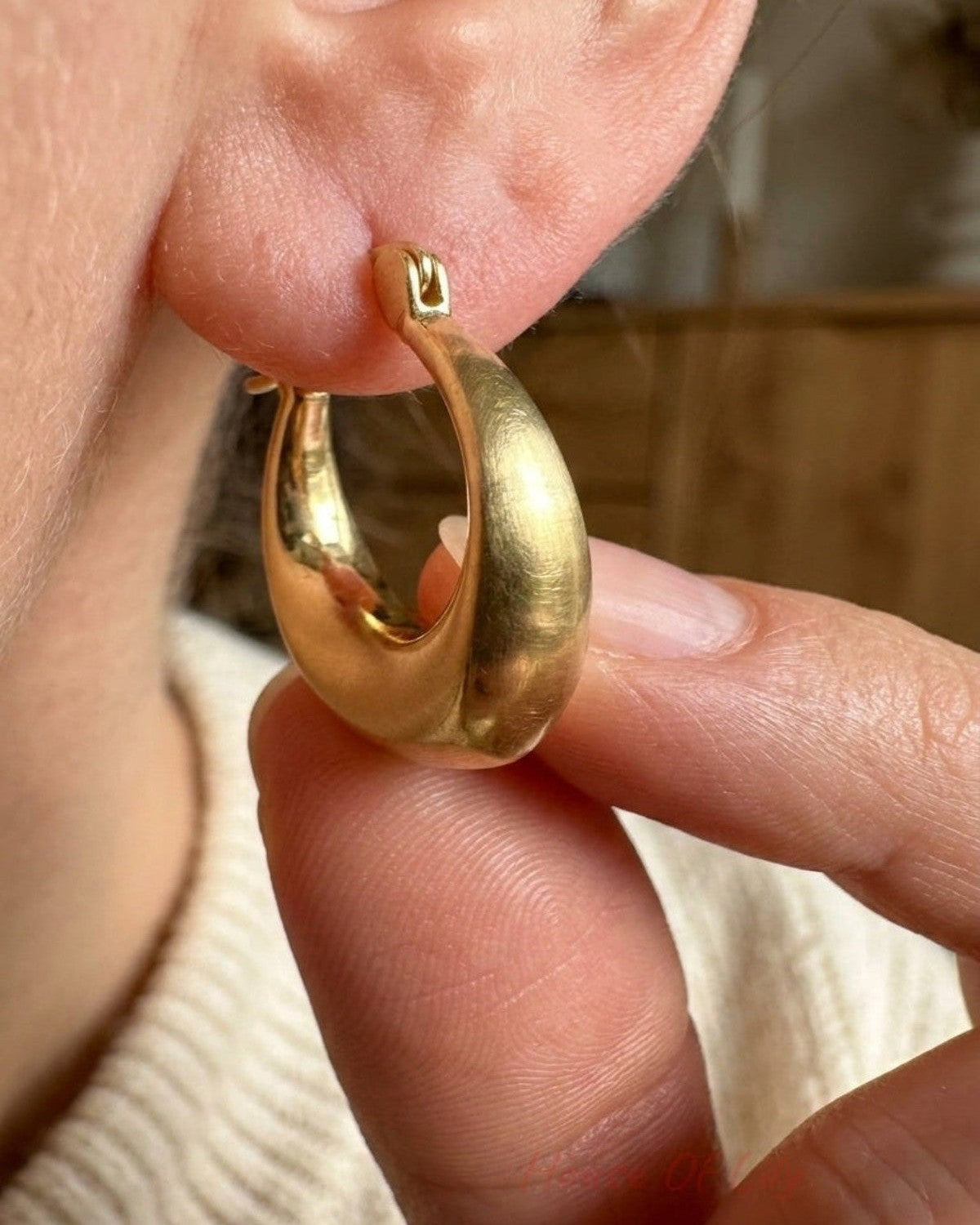Chunky, brushed gold hoop earring with an organic, curved, tapered shape worn in an earlobe.