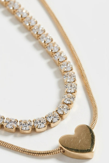 Layered gold necklace featuring a rhinestone strand and a smooth heart pendant on a chain.