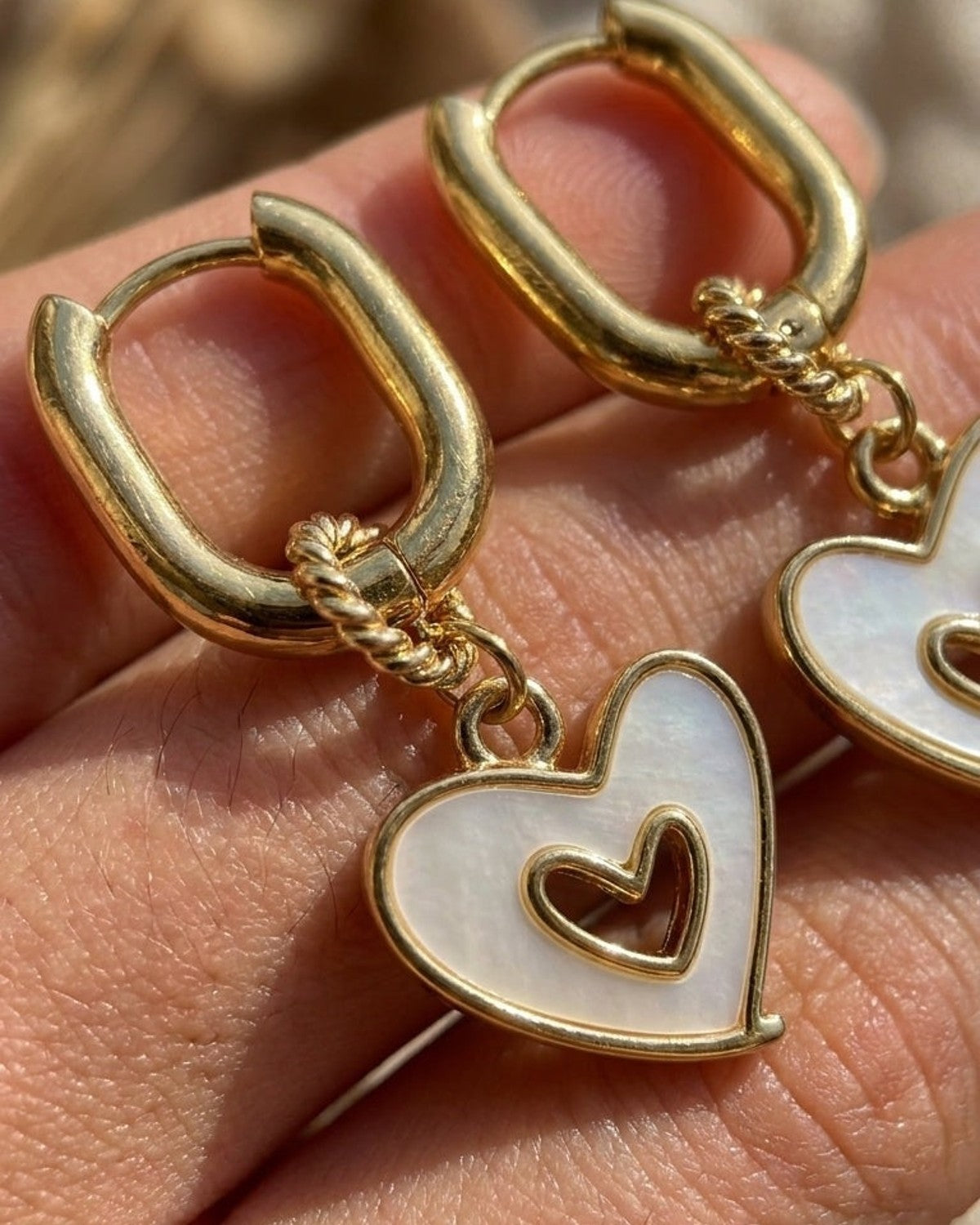 Gold huggie hoop earrings with mother-of-pearl heart drops containing a smaller gold heart.