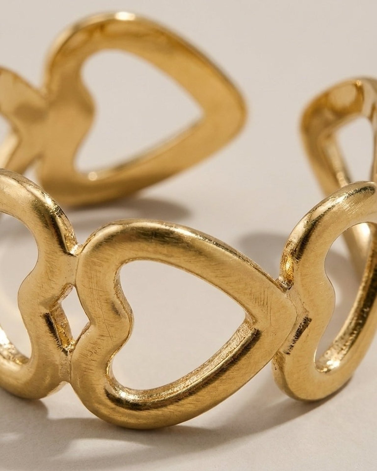 Gold metallic ring featuring a band formed by interconnected openwork heart shapes.
