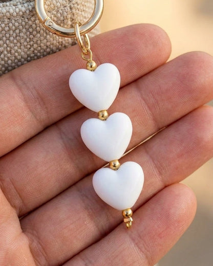 Gold-tone keychain with three smooth white heart charms and small gold spacer beads in a person's hand.