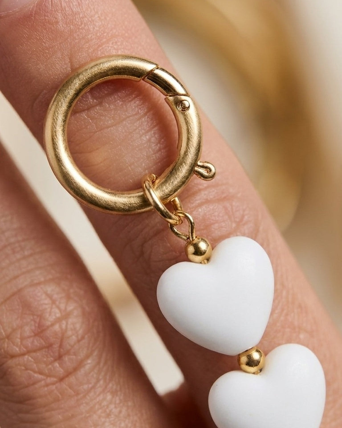 Gold clasp attached to a vertical strand of three white heart beads separated by small gold spheres.