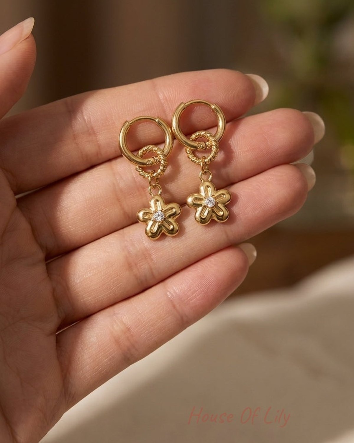 Gold huggie hoop earrings with a twisted ring and a dangling daisy charm featuring a central crystal stone.