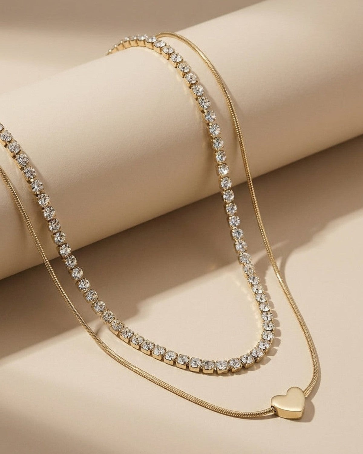Layered gold necklace featuring one rhinestone tennis chain and a smooth snake chain with a heart pendant.