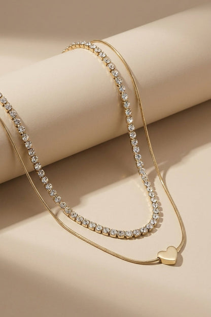 Layered gold necklace featuring one rhinestone tennis chain and a smooth snake chain with a heart pendant.