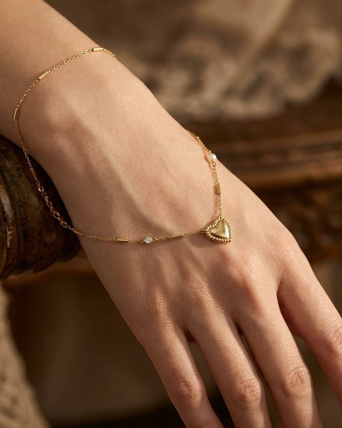 A gold heart pendant necklace with a beaded edge resting on a person's hand.