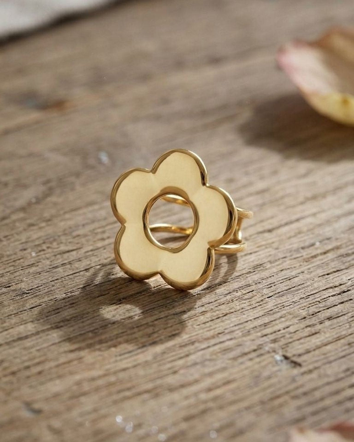 Delicate stainless steel Lily Flower Power statement ring with hollow centre, resting on rustic wooden surface in natural light, highlighting fine petal details.
