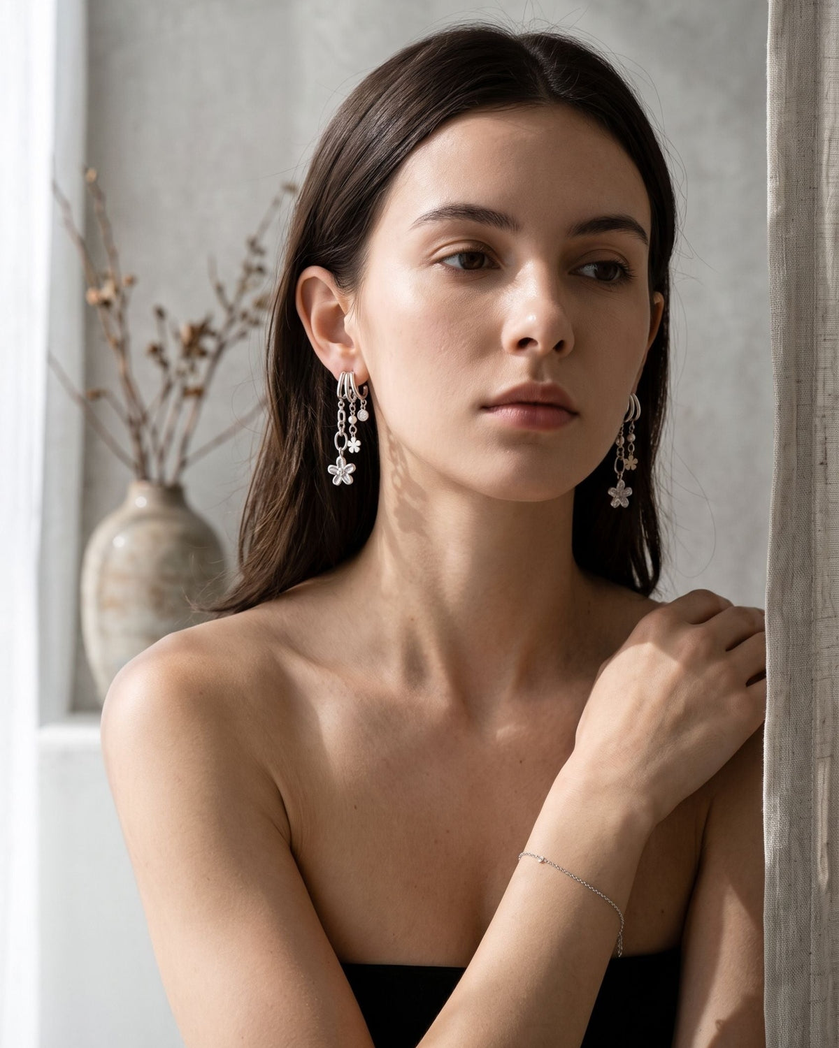 Delicate flower shaped drop earrings with zircon detail worn by a model in a minimalist setting.