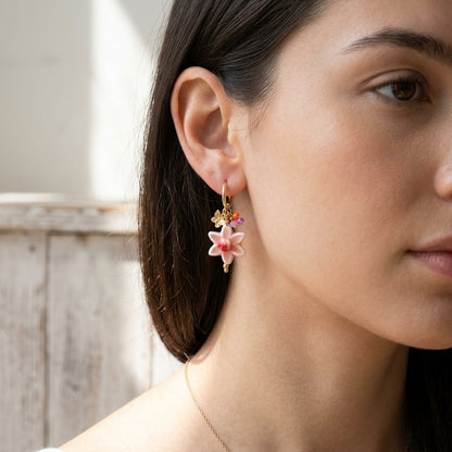 Close-up of flower-shaped drop earrings with ceramic and glass details, emphasizing the intricate craftsmanship and gold plating.