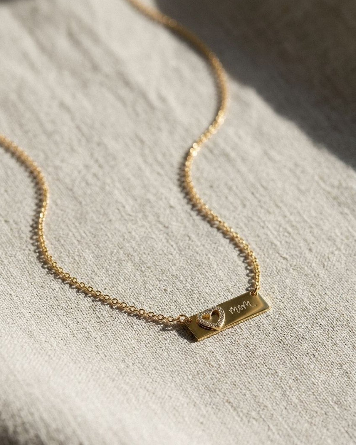 Small stainless steel heart pendant necklace resting on textured neutral linen fabric