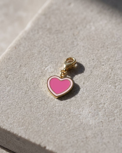 Small heart-shaped enamel charm on a gold-tone lobster clasp resting on a textured white stone surface.