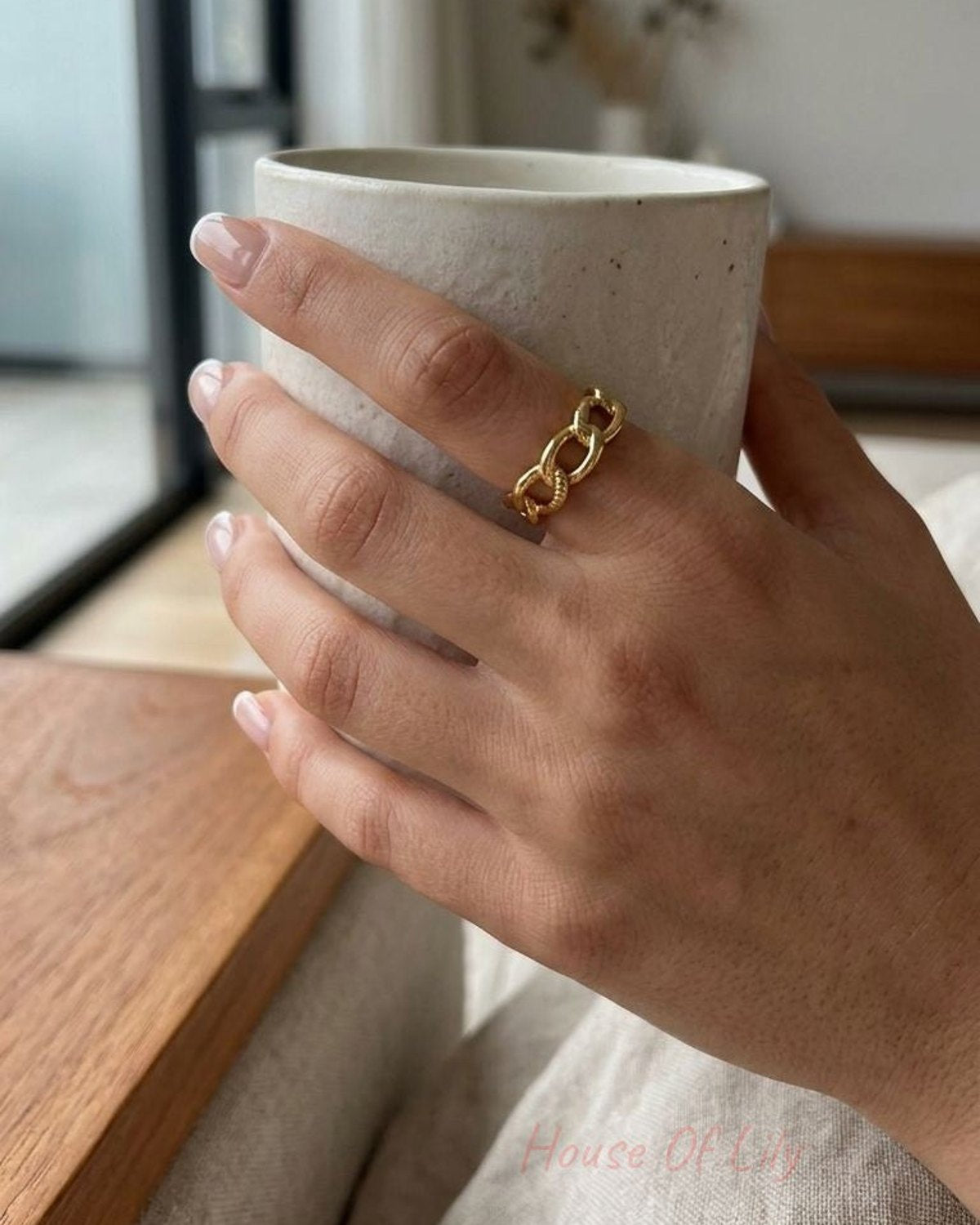Close-up of a small stainless steel ring with a chain pattern, showcasing its shiny finish and irregular links on a textured surface.