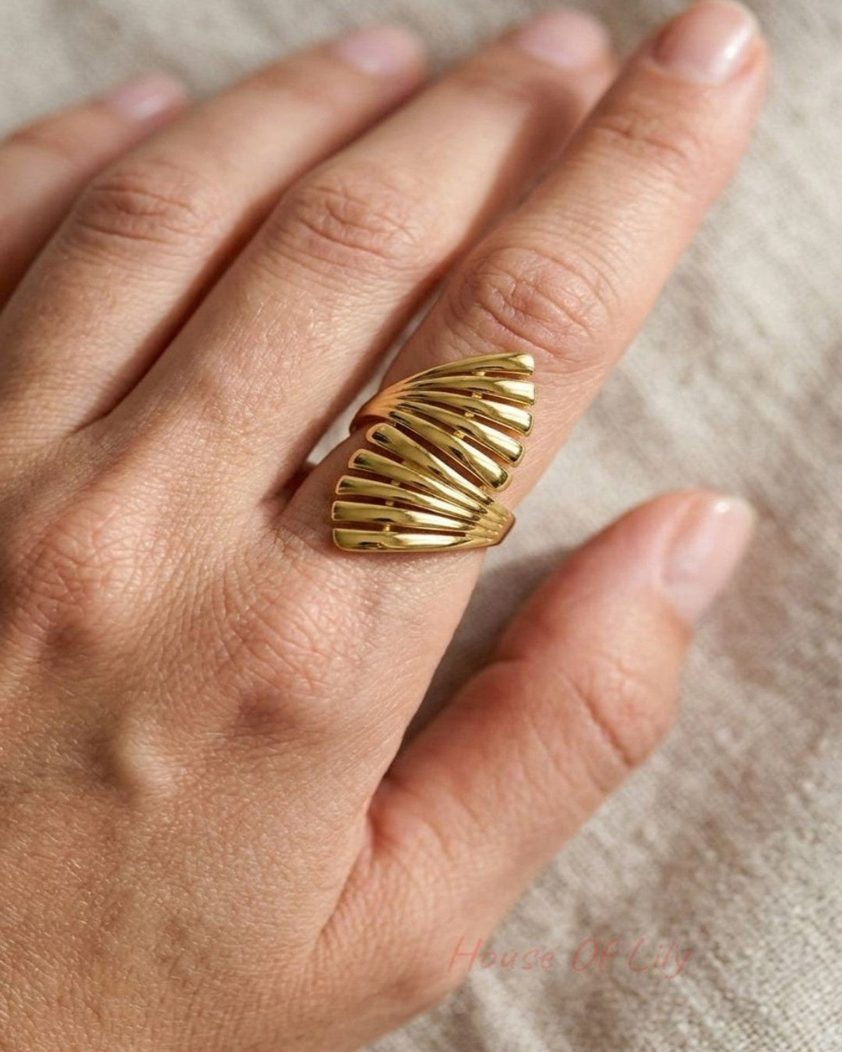 Close-up of the Sculpted Gold Statement ring on a slender finger, highlighting its organic wave pattern and high-shine gold finish in natural light.