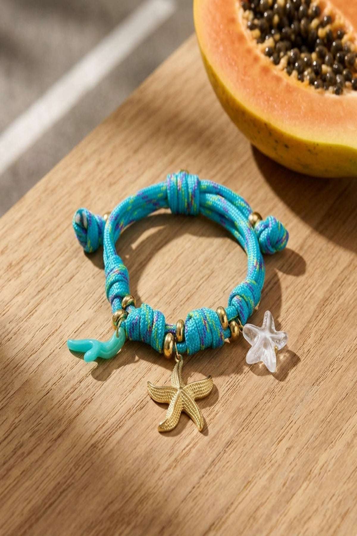 Delicate rope bracelet with starfish charms and knot details, featuring stainless steel and acrylic components, resting on a wooden surface.
