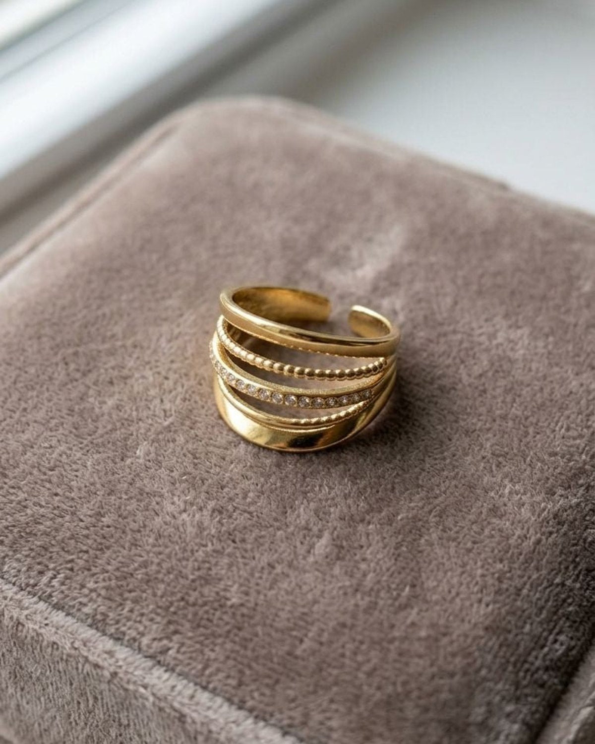 Delicate stacked Glamour Lily ring with gold-tone metal bands on a neutral velvet surface, showcasing minimalist open-band style and craftsmanship.