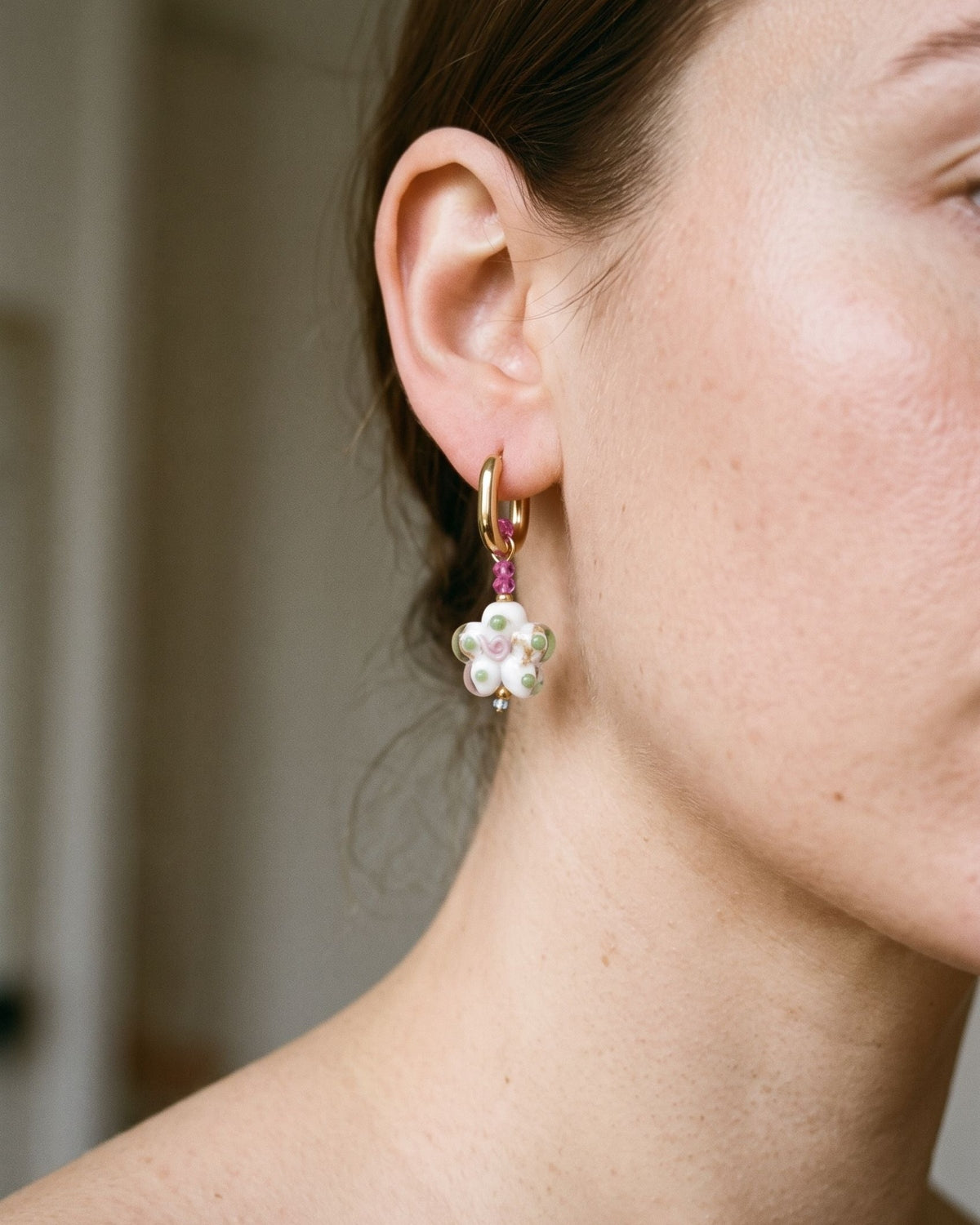Stainless steel hoop earrings featuring delicate flower-shaped crystal pendants resting on a textured ceramic surface.