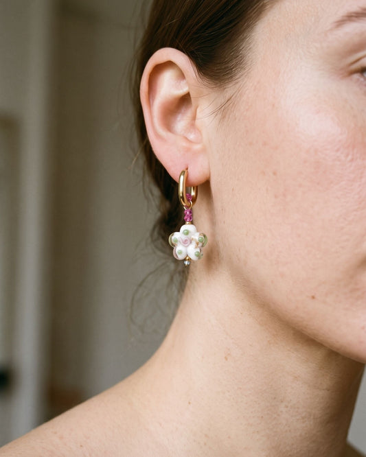 Stainless steel hoop earrings featuring delicate flower-shaped crystal pendants resting on a textured ceramic surface.