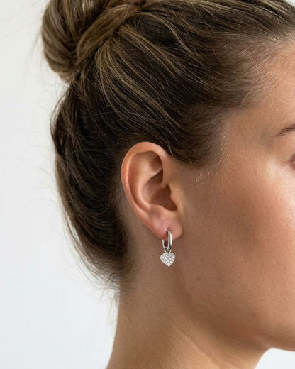 Woman wearing petite stainless steel heart drop earrings with clear pavé zircon inlay for a delicate everyday look.