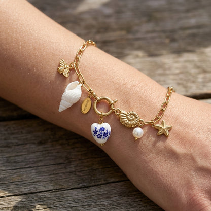 Delicate stainless steel charm bracelet with starfish seashells and ocean motifs on a natural wood surface