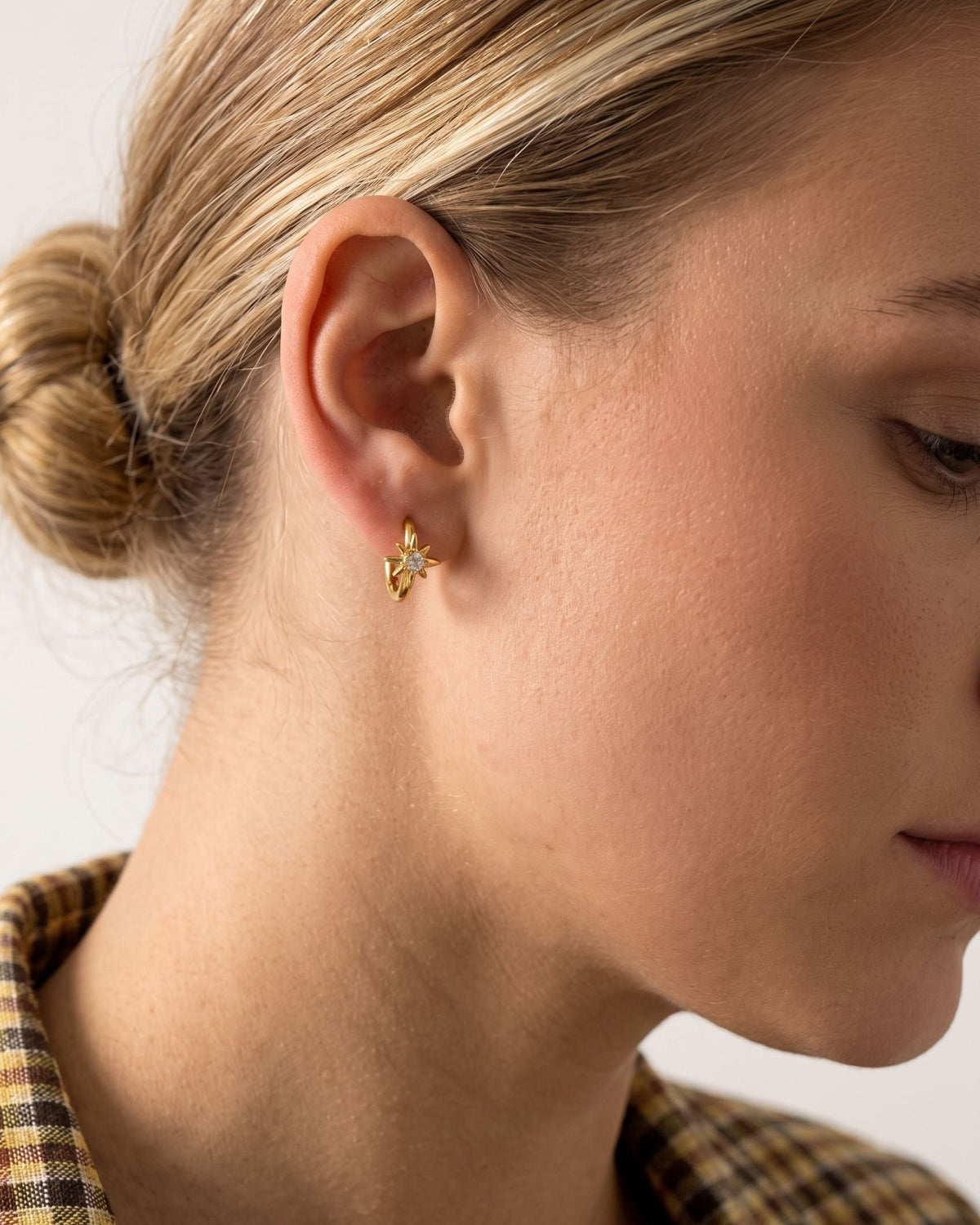 Delicate hoop earrings featuring a small star charm with a sparkling zircon stone worn on an earlobe.