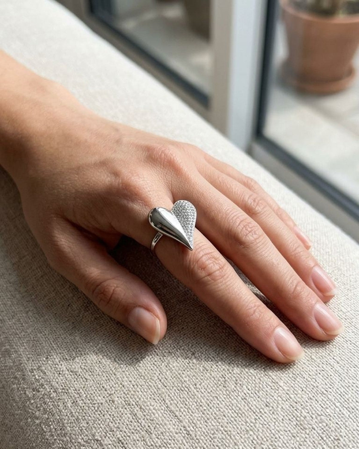 Model wearing the Bold Heart Statement Ring on her finger, resting on linen fabric with natural light emphasizing its sparkle and stainless steel shine.