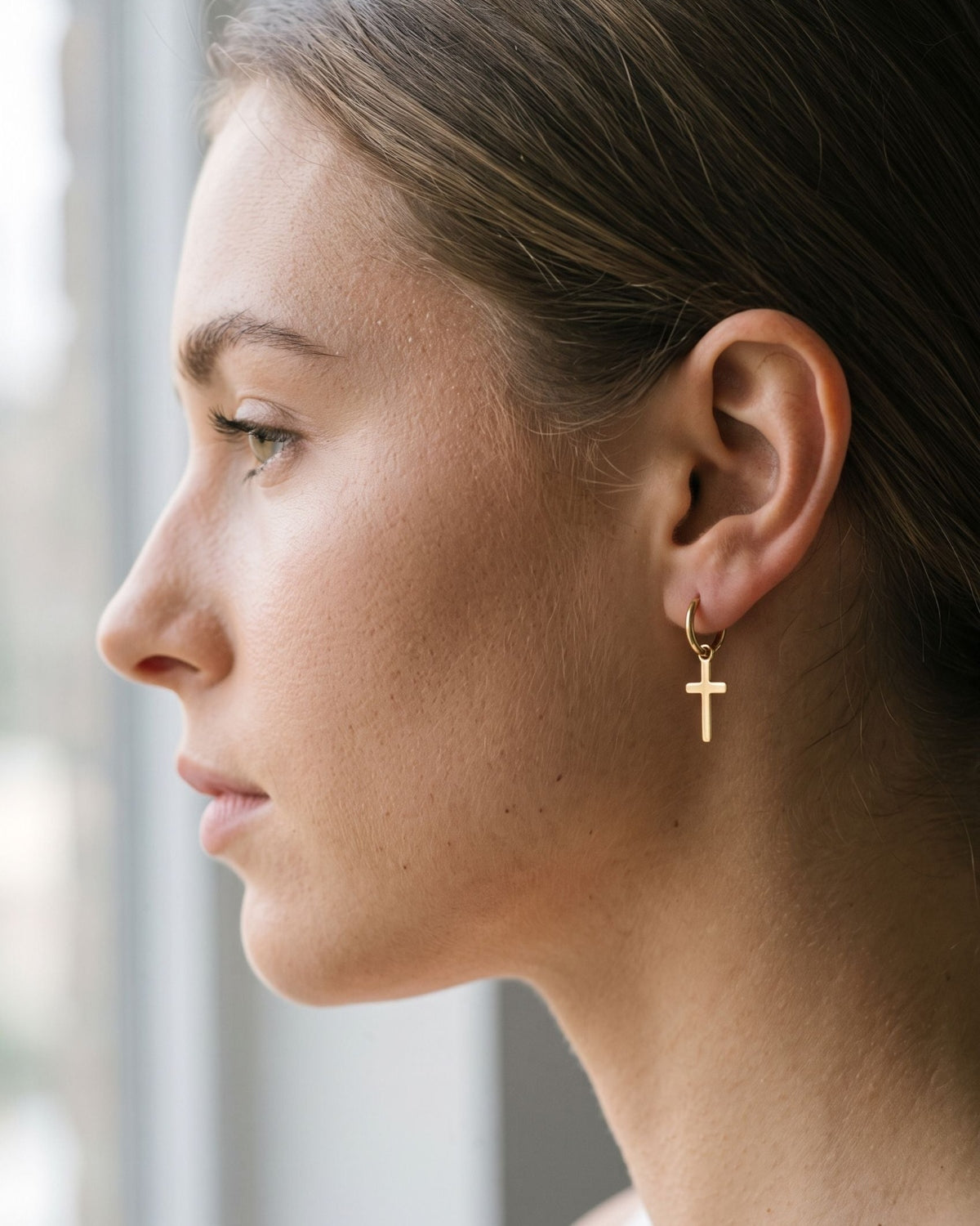 A woman wearing minimalist stainless steel cross drop earrings with a simple loop connector for everyday style.