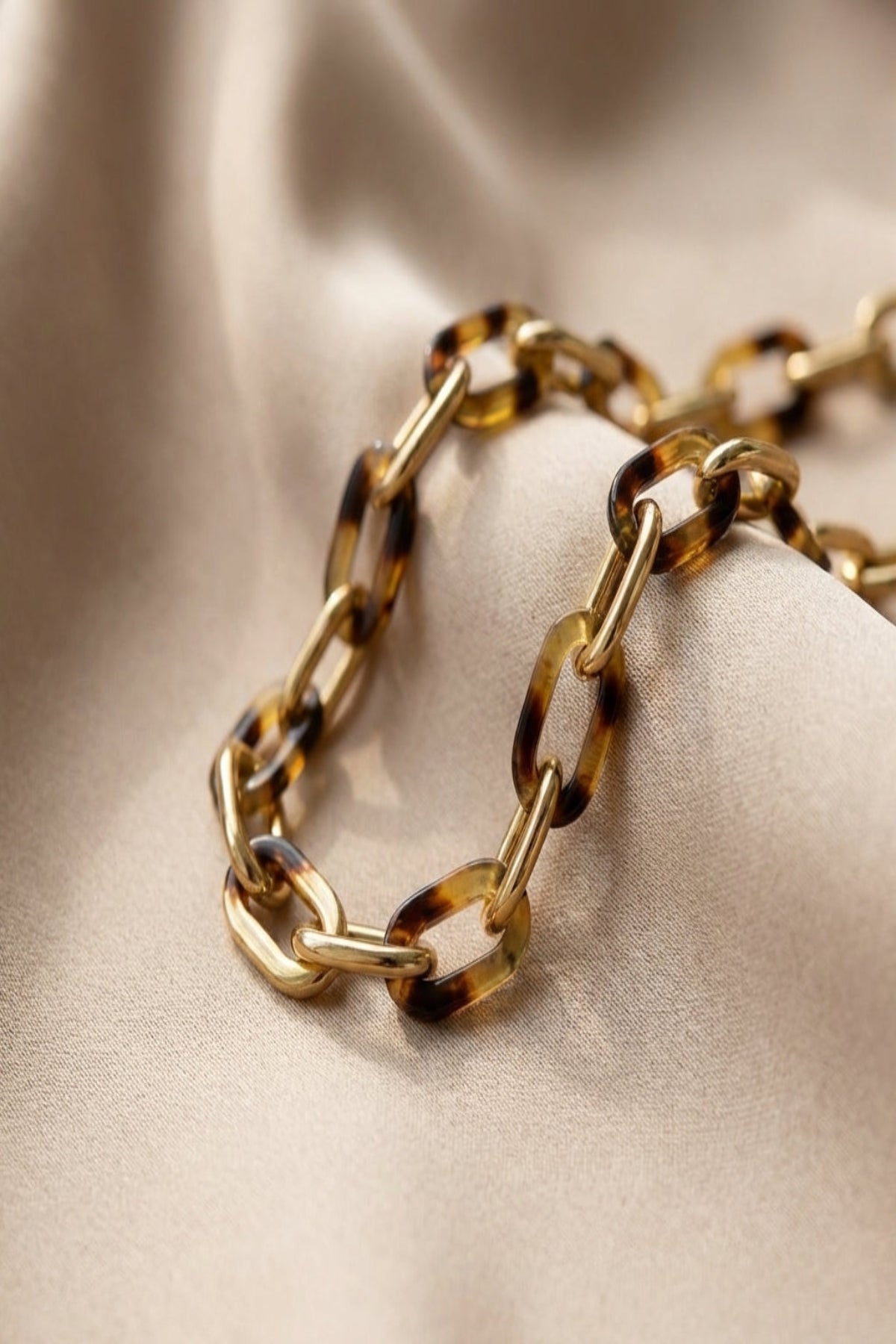 Close-up of a glossy gold-tone tortoise link chain necklace highlighting detailed textures and subtle color variations on a neutral fabric background.