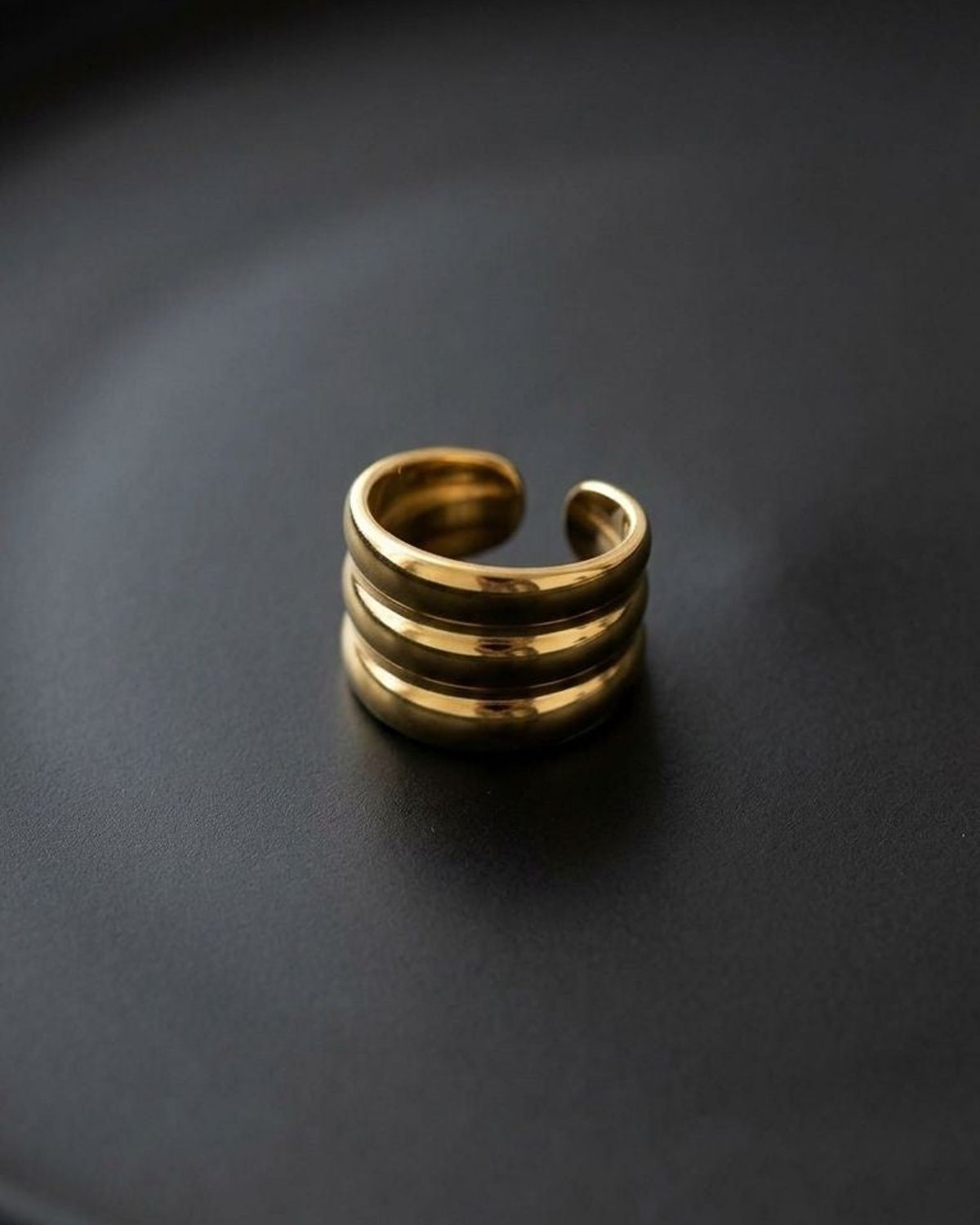 Close-up of Triple Stack Gold ring on matte black surface highlighting sculptural interlayer design.