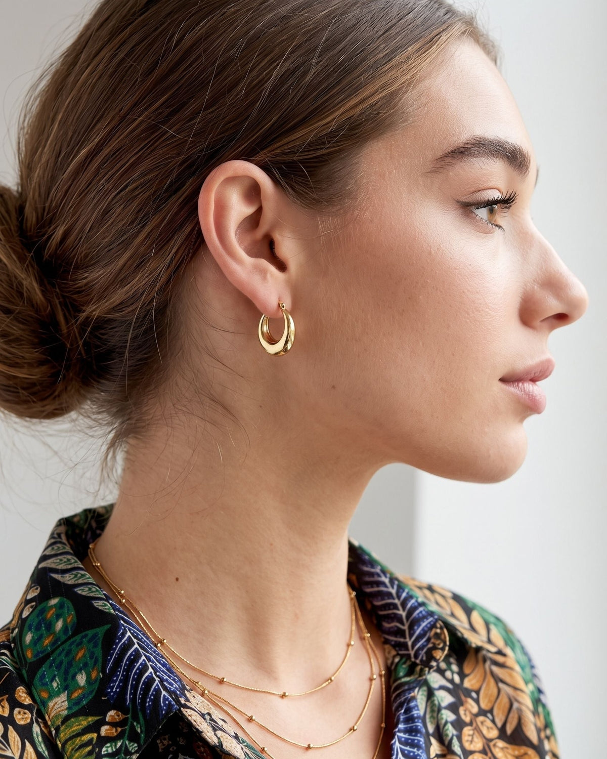 Model wearing delicate two-tone hoop earrings with natural side lighting highlighting the polished metallic finish.