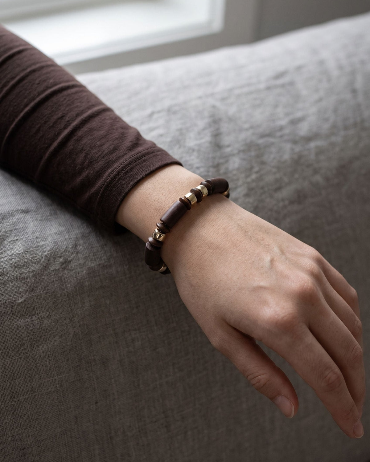 Unisex retro wooden beaded bracelet worn on a wrist with a dark long-sleeved top against a soft linen background.