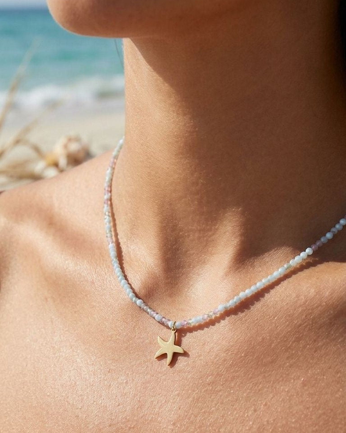 Close-up of the vibrant beaded necklace featuring a stainless steel starfish charm on a model's neck, highlighting the colorful beads and beach setting.